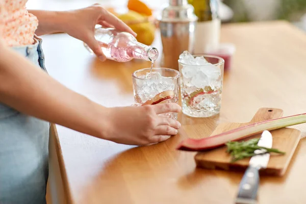 飲み物と人々のコンセプト 自宅のキッチンでルバーブと氷でカクテルを作る強壮剤の水を持つ女性のクローズアップ — ストック写真