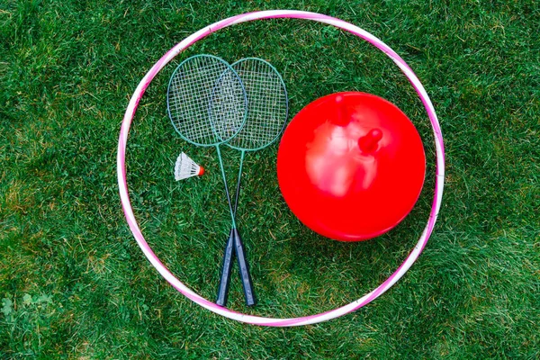 leisure games, sport equipment and toys concept - bouncing ball or hopper, hula hoop and set of badminton rackets with shuttlecock on grass