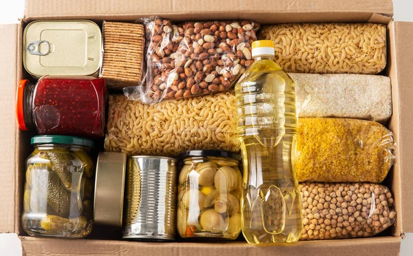 food storage, donation and eating concept - close up of box with groceries and preserves on white background, top view