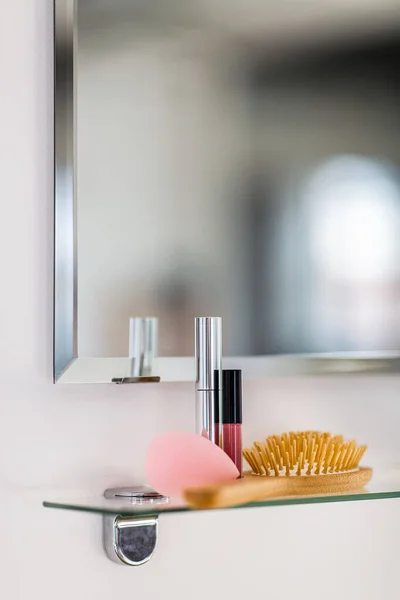 hygiene, beauty and daily routine concept - close up of hairbrush and cosmetics on mirror shelf in bathroom