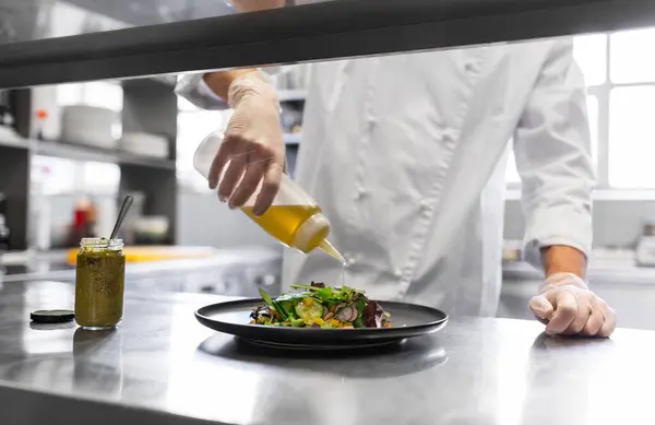 人々のコンセプト レストランのキッチンテーブルでオリーブオイルと野菜サラダのドレッシングプレートを調理男性シェフの終わり — ストック写真