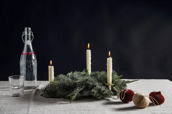 冬休みやお祝いのコンセプト 火の花輪 クリスマスのおもちゃ 水のガラス瓶 黒い背景の上にテーブルに燃えるろうそく — ストック写真