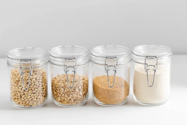 food, culinary and storage concept - jars with oat flakes, semolina, couscous and beans on white background