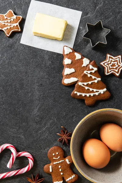 christmas, food cooking and winter holidays concept - close up of iced gingerbread cookies, molds, flour and other ingredients on black table top at kitchen
