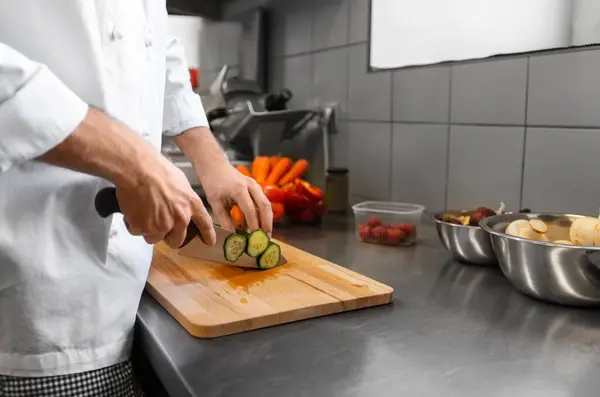 人々の概念 レストランキッチンでまな板の上にキュウリを切るナイフで男性シェフの終わり — ストック写真