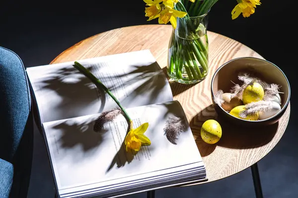 室内装潢 节假日和室内装潢概念 将现代蓝色椅子 碗中的彩蛋 水仙花和杂志放在黑暗房间的桌子上 — 图库照片#