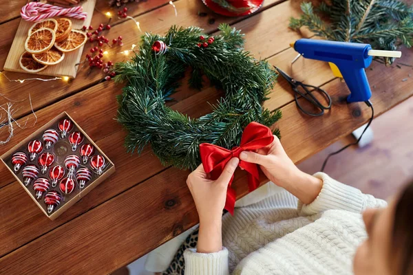 stock image winter holidays, diy and hobby concept - close up of woman with red bow decoration making fir christmas wreath at home