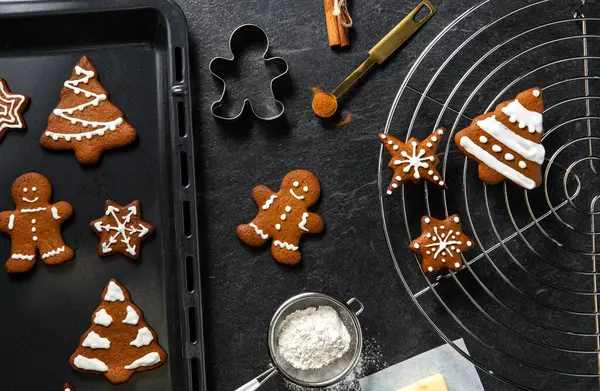 christmas, food cooking and winter holidays concept - close up of iced gingerbread cookies, molds, flour and oven tray on black table top at kitchen