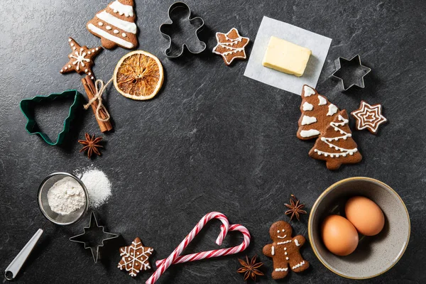 christmas, food cooking and winter holidays concept - close up of iced gingerbread cookies, molds, flour and other ingredients on black table top at kitchen