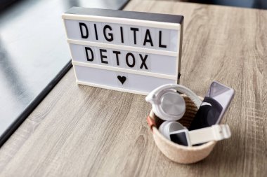technology concept - digital detox words on light box and different gadgets on blue background clipart