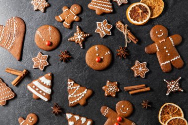 baking, cooking, christmas and food concept - close up of iced gingerbread cookies, cinnamon and star anise on black table top clipart