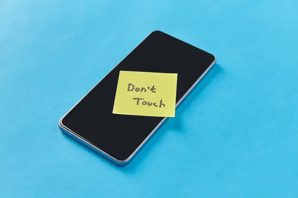 privacy, technology and digital detox concept - close up of smartphone with dont touch words on sticky note on blue background