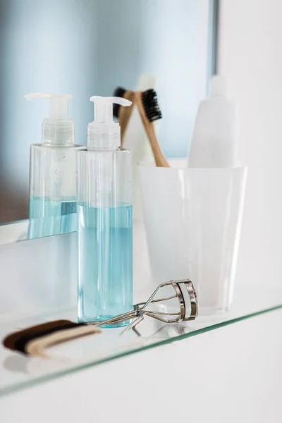 hygiene, beauty and daily routine concept - close up of lotion, toothbrush and toothpaste on mirror shelf in bathroom