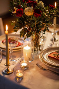 holidays, romantic date and celebration concept - close up of festive table serving for two with flowers in vase and candles burning at home on valentines day clipart