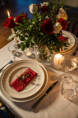 holidays, romantic date and celebration concept - close up of festive table serving for two with flowers in vase and candles burning at home on valentines day clipart