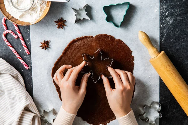 ベーキング クリスマスのコンセプト 黒いキッチンテーブルの上に金型切削ジンジャーブレッド生地で手を閉じる — ストック写真