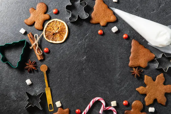christmas, food cooking and winter holidays concept - close up of gingerbread cookies, molds, pastry bag and other ingredients on black table top at kitchen