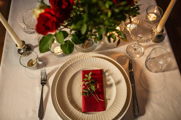 holidays, dinner party and celebration concept - close up of festive table serving with flowers in vase and candles burning at home on valentines day