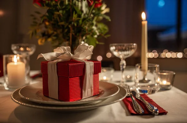holidays, dinner party and celebration concept - close up of festive table serving with gift box, flowers in vase and candles burning at home on valentines day