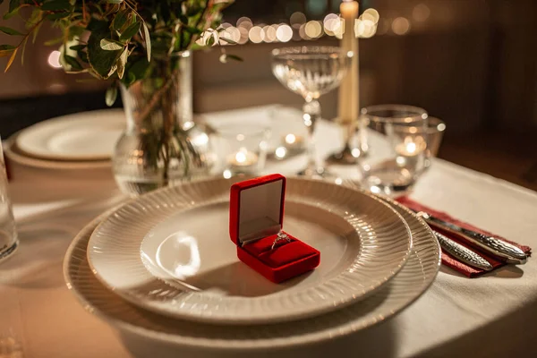 节假日 情人节和求婚理念 在餐桌上放上红盒的订婚戒指 两个人一起享用 花瓶里放着花 家里点着蜡烛 — 图库照片