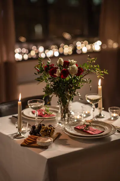 holidays, romantic date and celebration concept - close up of festive table serving for two with flowers in vase and candles burning at home on valentines day at home