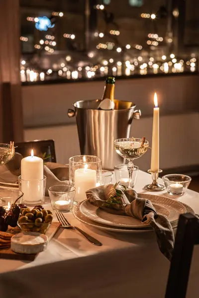 holidays, dinner party and celebration concept - close up of festive table serving for two with champagne bottle in ice bucket and candles burning at home on valentines day