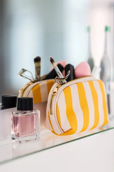 hygiene, beauty and daily routine concept - close up of cosmetic bag with make-up stuff and perfume on mirror shelf in bathroom