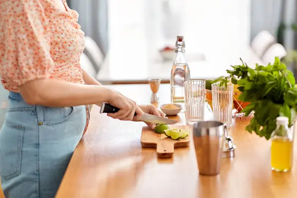 飲み物と人々のコンセプト ナイフでライムを切断し 自宅のキッチンでカクテルを作る女性のクローズアップ — ストック写真