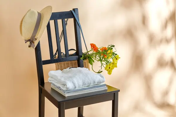 家居装饰和设计理念 在米色背景上的老式椅子上的柳条袋或篮子 帽子和杂志中的花朵 图库图片