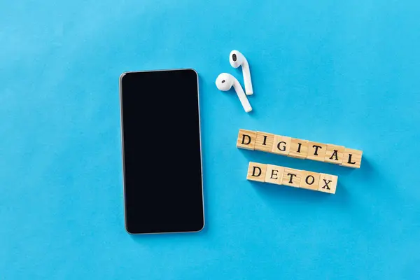 デジタルデトックスとテクノロジーコンセプト スマートフォン ワイヤレスイヤホン 木製のおもちゃブロックまたはブルーバックグラウンドのスタンプ ストック写真