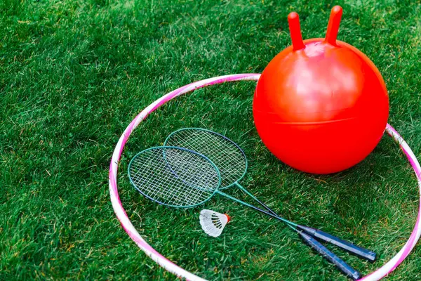 leisure games, sport equipment and toys concept - bouncing ball or hopper, hula hoop and set of badminton rackets with shuttlecock on grass