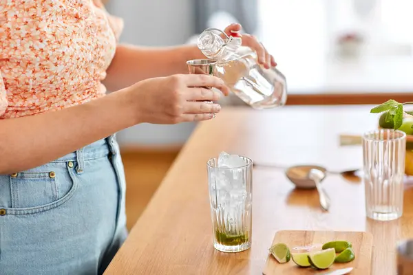 飲み物と人々のコンセプト 家庭のキッチンでガラス瓶から水を注ぐ女性の閉じるとリムモヒートカクテルを作る ロイヤリティフリーのストック写真