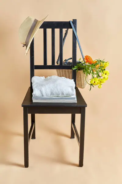 家居装饰和设计理念 在米色背景上的老式椅子上的柳条袋或篮子 帽子和杂志中的花朵 免版税图库照片