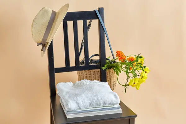 家居装饰和设计理念 在米色背景上的老式椅子上的柳条袋或篮子 帽子和杂志中的花朵 图库图片