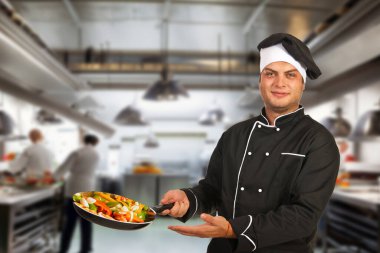 Adult chef in cafe kitchen, dressed in uniform, working on food preparation. clipart