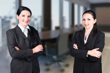 Resmi giyinmiş, kollarını kavuşturmuş, gülümseyen ve kameraya bakan iki kendine güvenen profesyonel..