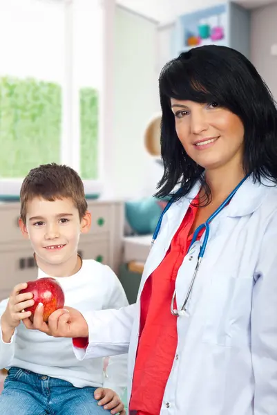 Szczęśliwa Pani Doktor Daje Czerwone Jabłko Uśmiechniętemu Dziecku Brakującymi Zębami — Zdjęcie stockowe