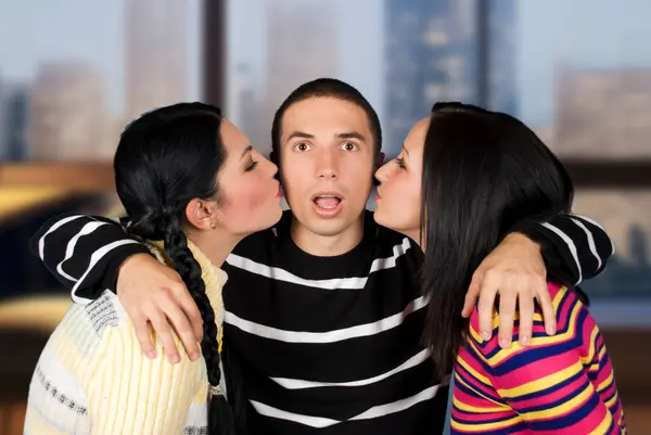 Young man looking surprised when two women kissing his cheeks,they wearing colorful sweaters on blue background