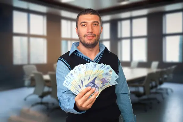 一个自信的年轻人在会议室里拿着罗马尼亚的钱 象征着金融讨论和商业文化的多样性 图库图片