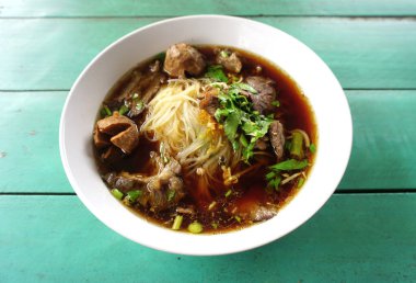 Yeşil masa arkasında haşlanmış domuz çorbası ile erişte.