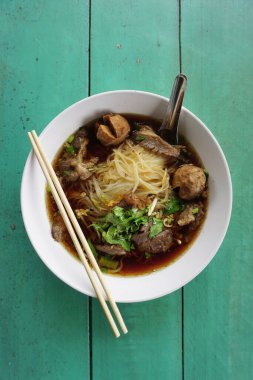 Yeşil masa arkasında haşlanmış domuz çorbası ile erişte.