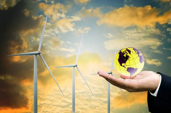 緑のエネルギーと持続可能な概念 ビジネスマンの手は日没の空の背景と世界と風力タービンを保持します — ストック写真