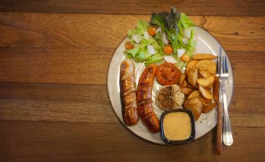 Salata ve patates cipsiyle ızgara Alman sosisi, ahşap masa arkası manzaralı üst manzara.