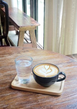 Latte kahve ve taze içme suyu. Ahşap tepside, arka planda.