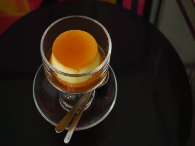 Karamelli muhallebi, cam bardakta, siyah masada, el kamerasıyla.