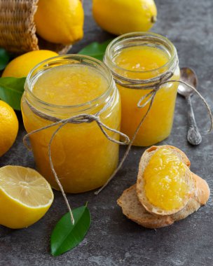 Cam kavanozlarda taze ev yapımı limon reçeli. Olgun limonlu masa ve reçelli ekmek dilimleri.