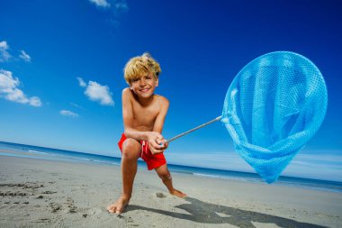 Low angle portrait young boy stand with butterfly nets lean catching critters on the sand ocean beach during tide