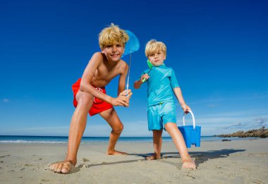 Low angle portrait of two young boys stand with butterfly nets lean catching critters on the sand ocean beach during tide