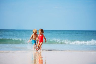 Cute little boy and a girl play with the ball in the ocean waves at the sand beach during summer vacation