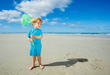 Cute blond boy stand with butterfly net on the sand beach catching crabs during tide at French Atlantic coast